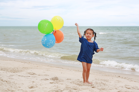 Happy little girl playing colorful balloons on the beach during summer vacation.の写真素材
