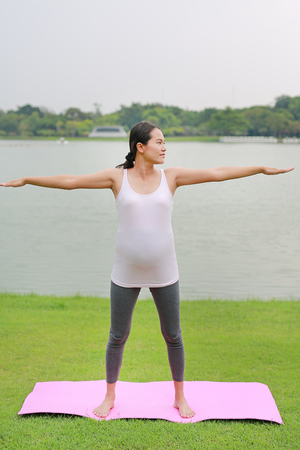 Beautiful Asian pregnant mother doing yoga in the public park near a lake.の写真素材