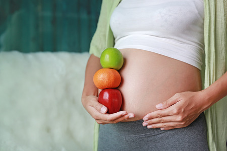 Pregnant woman holding Green-Red Apple and Orange fruit at her tummy. Dieting Concept.