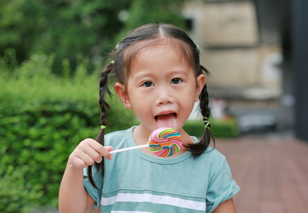 Close up little girl licking lollipop candy in the garden