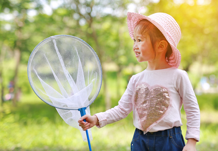 Adorable little asian girl wear straw hat in a field with insect net in summer. Outdoor activity.の写真素材