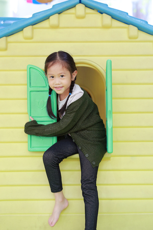 Adorable little Asian child girl playing with window toy playhouse in playground.の写真素材