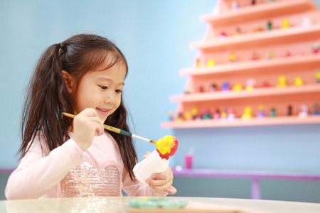 Happy little child girl having fun to paint on stucco doll indoor.の写真素材