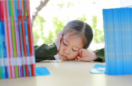 Tired little Asian girl lying on bookshelf at library. Education concept.の写真素材