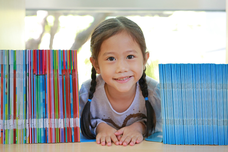 Happy little Asian child girl lying on bookshelf at library. Children creativity and imagination concept.の写真素材