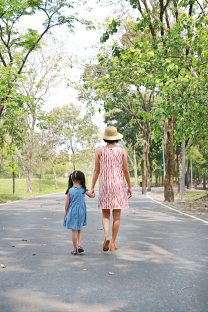 Mother and her daughter walking on the road and holding hands in the outdoor nature garden. Back view.の写真素材