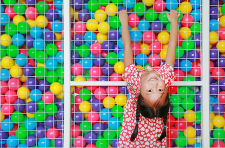 Smiling little Asian child girl playing climb and hanging on cage of playground colorful toy ball with looking camera.の写真素材