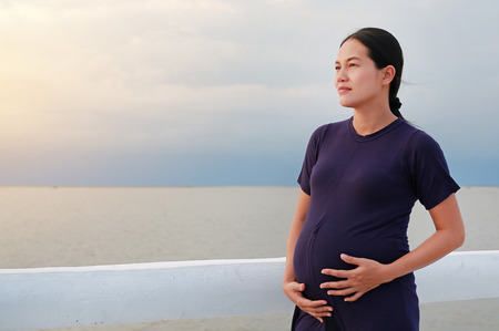 Beautiful pregnant woman standing on seashore with looking out.の写真素材