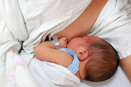 Close-up infant baby feeding from mother breastfeeding her newborn child on the hospital bed.の写真素材