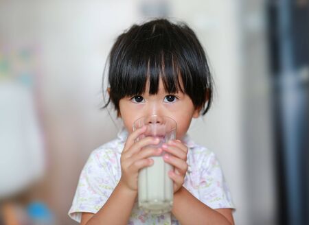 Cute Little girl in pajamas drinking milk from glass indoor at the morning.の写真素材