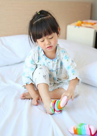 Lovely little asian girl trying to put a socks on the bed.の写真素材