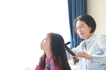Beautiful little Asian child girl with long hair and mom dressed up for Smooth hair at morning in the room.の写真素材
