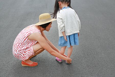 Asian mother helping her little daughter to put shoes on the road outdoor.の写真素材