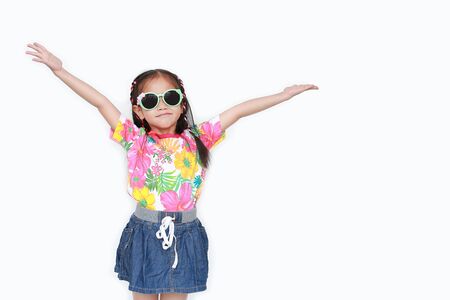 Portrait of happy little Asian kid girl stretch arms wide open up wearing a floral pattern summer dress and sunglasses isolated on white background with copy space. Summer and fashion concept.の写真素材