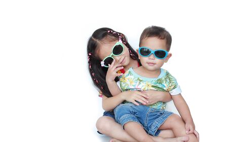 Portrait little Asian sister embracing little brother wearing a flowers summer dress and sunglasses isolated on white background. Summer and fashion concept.の写真素材