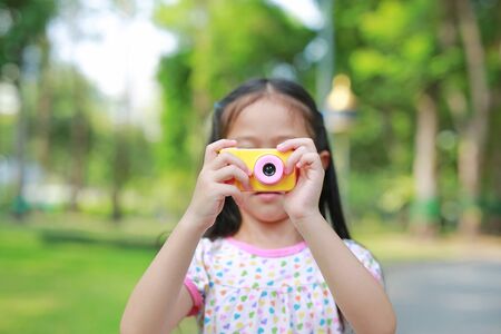 Close-up little girl with digital camera toy in the garden outdoor. Focus at camera in hands.の写真素材