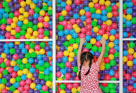 Little Asian kid girl playing climb on cage of playground colorful toy ball. Rear view.の写真素材