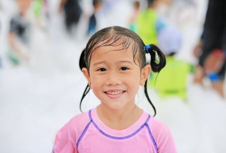 Close-up cute little Asian child girl smiling having fun in Foam Party at the pool outdoor.の写真素材