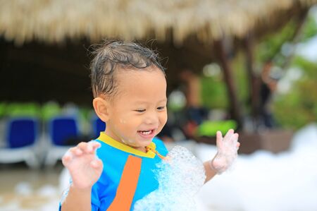 Portraits of little Asian baby boy smiling having fun in Foam Party at the pool outdoor.の写真素材