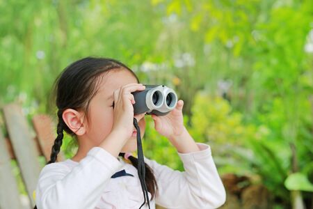 Little child girl in a field looking through binoculars in nature outdoor. Explore and adventure concept.の写真素材