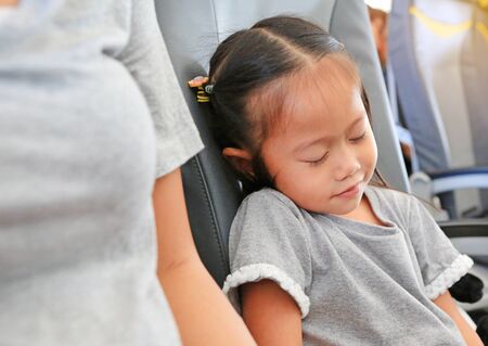 Cute little Asian child girl sleeping on the seat of airplane beside her mother.の写真素材