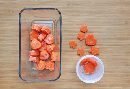 Frozen baby food homemade, Orange heart from carrot Cubes in square glass bowl on wooden board.