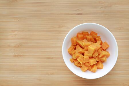 Boil chopped sweet potatoes in white bowl against wooden board background with copy space.の写真素材