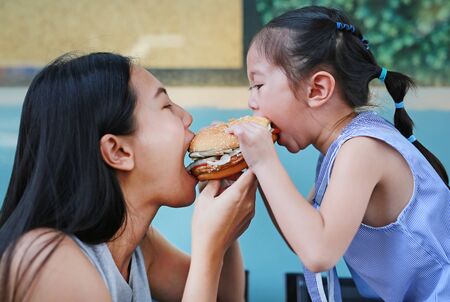 Close up Asian mother with child girl eating a hamburger together.の写真素材