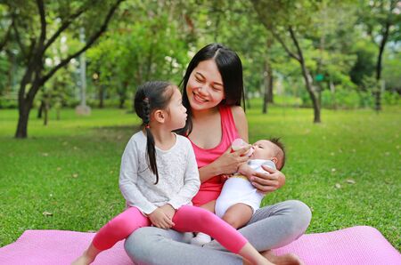 Family of mother feeding milk infant from bottle with take care her daughter lying in the garden.の写真素材