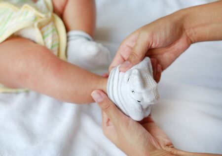 Close-up mother hands trying to put a socks for her infant baby on the bed.