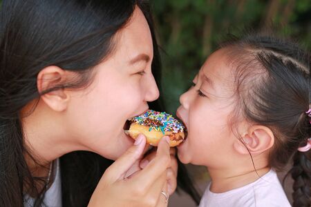Close up Asian mother and her daughter eating rainbow donut together.の写真素材