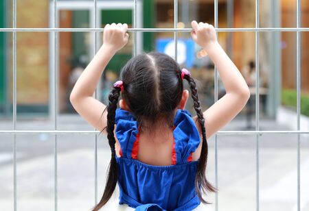 Back view of child girl holding steel fence.の写真素材