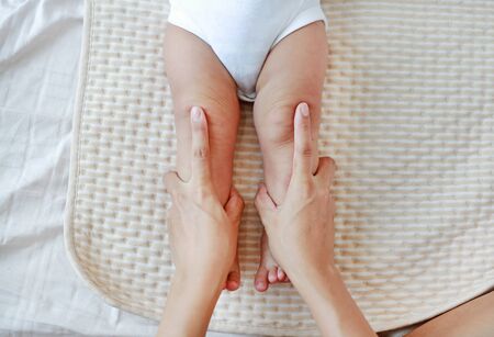 Mother hand massaging to leg of infant baby on the bed at home.