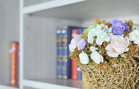 Closeup beautiful artificial rose flower in basket on the bookshelf in library.