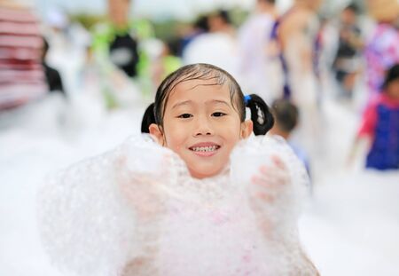 Close-up cute little Asian child girl smiling having fun in Foam Party at the pool outdoor.の写真素材