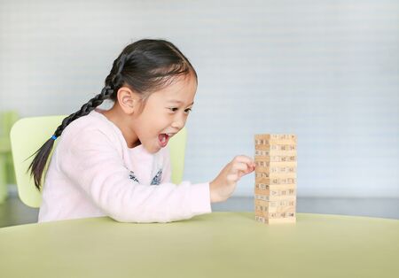 Happy little Asian child girl playing wood blocks tower game for Brain and Physical development skill in a classroom. Focus at children face. Kid imagination and learning concept.の写真素材