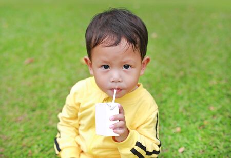 Portrait of little baby boy in sport cloth drinking milk from box with straw in the garden.の写真素材