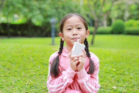 Portrait of little girl in sport cloth drinking milk from box with straw in the nature park.の写真素材