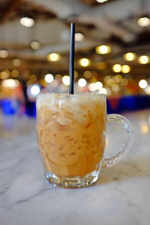 Iced Thai milk tea glass cup on table against department store background.