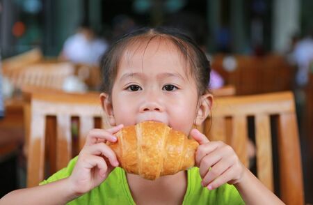 Asian little girl eating croissant at restaurantの写真素材
