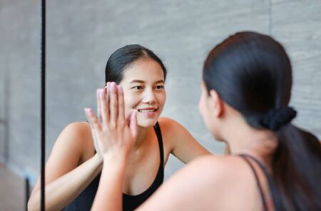 Face of smiling young asian woman looking at her reflection in mirror to camera.の写真素材