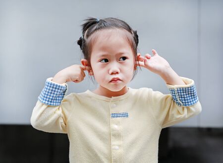 Cute little child girl shutting down her ears, holding her hands covers ears not to hear.の写真素材