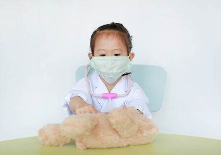 Asian Kid girl with protect mask plays doctor with her bear doll.の写真素材