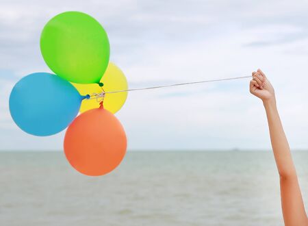 Hand holds a bunch of balloons on the beach background