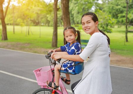 Asian mother and daughter riding bicycle together in park.の写真素材