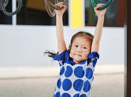 Cute asian girl playing on gymnastic ring with looking at camera.