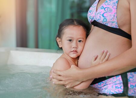 Little child girl listening belly of pregnant women in hot tub.の写真素材