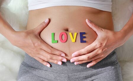 Close up Pregnant woman sitting on soft sofa and touching her belly with sign LOVE in front of her belly.の写真素材