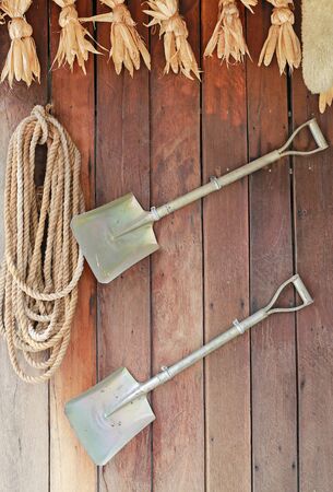 Shovel and rope hanging on the wooden plank wall. Garden decoration. Gardening tools.の写真素材