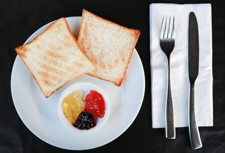 Toast with jam on white plate on the black table.